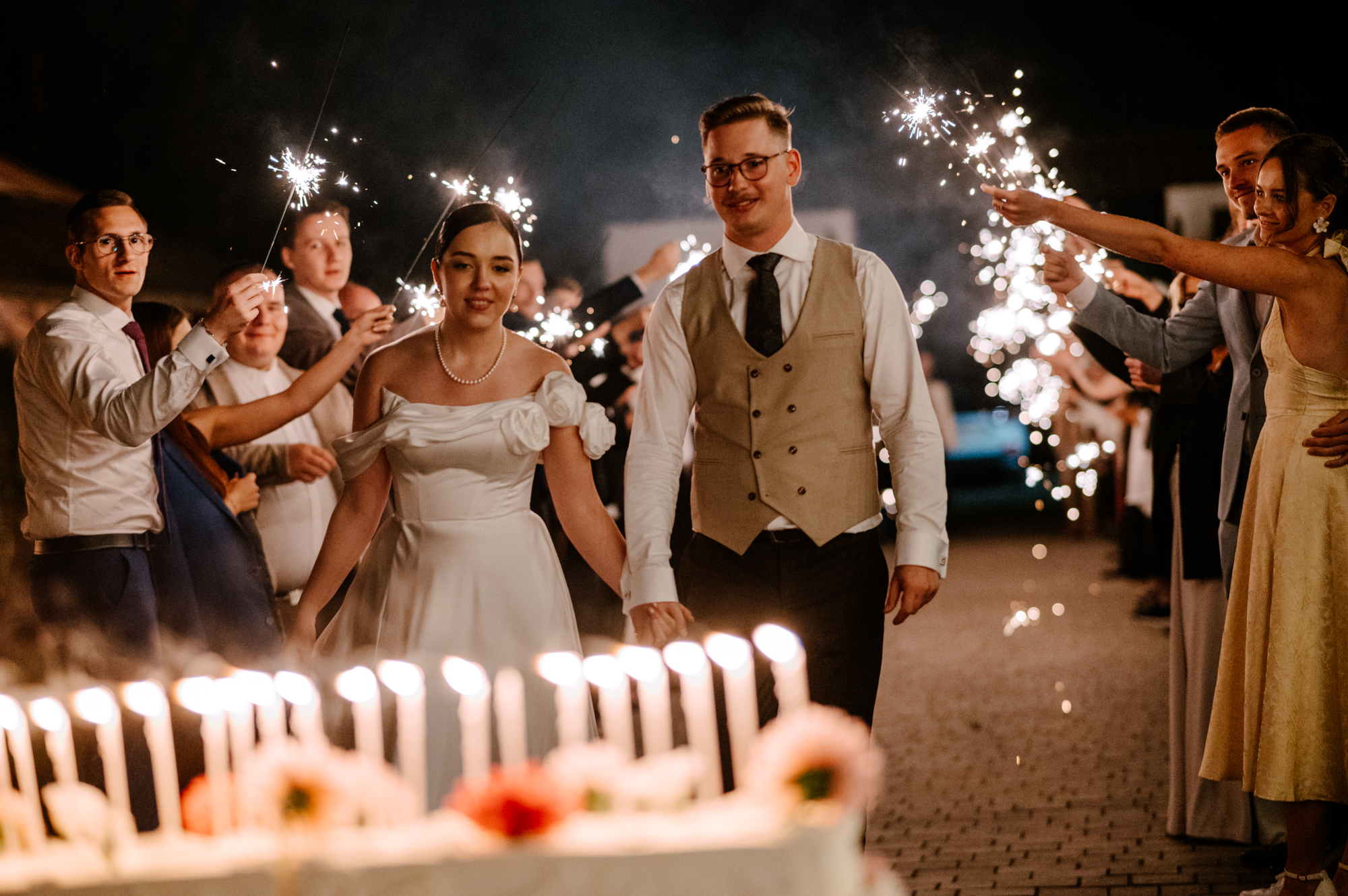 Karolina i Patryk przechodzący wśród gości trzymających zimne ognie podczas wesela